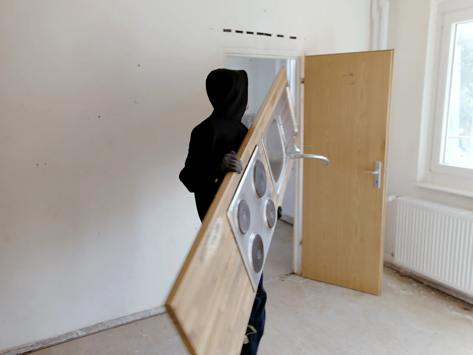 Mitarbeiter von Sorglos Entrümpeln im schwarzen Hoodie trägt eine ausgebaute Küchenarbeitsplatte mit Kochfeld aus einer leeren Mietwohnung