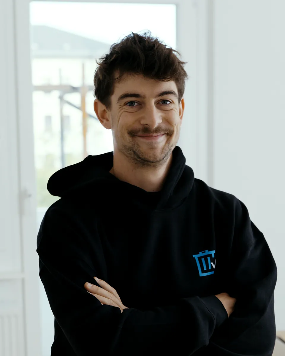 Silas Mecklenburg von Sorglos Entrümpeln mit dunklen Locken im schwarzen Kapuzenpullover mit Sorglos-Logo, die Arme verschränkt
