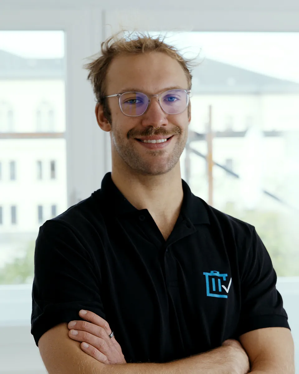 Marvin Kleß von Sorglos Entrümpeln mit Brille im schwarzen Poloshirt mit Sorglos-Logo, die Arme verschränkt