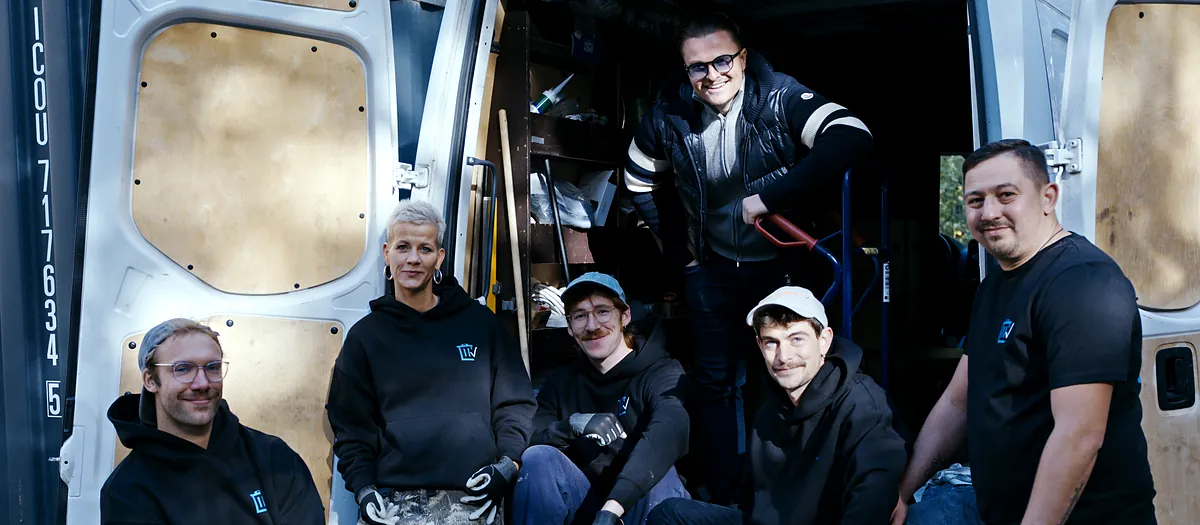 Das Team von Sorglos Entrümpeln sitzt im offenen Transporter, oben im Laderaum steht Inhaber Ruben Bestfleisch