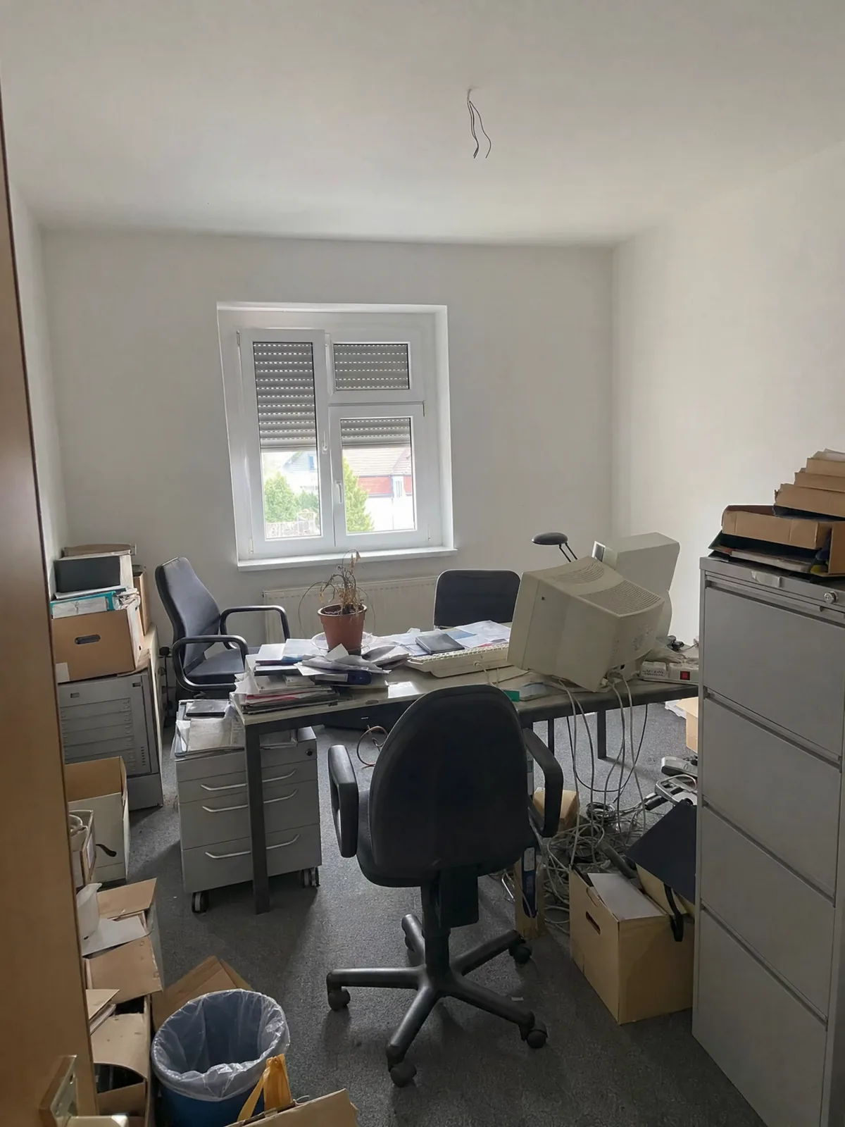 Büroraum vor der Auflösung: Schreibtische mit Kabeln, Bürostühle, Aktenschränke und gestapelte Kartons