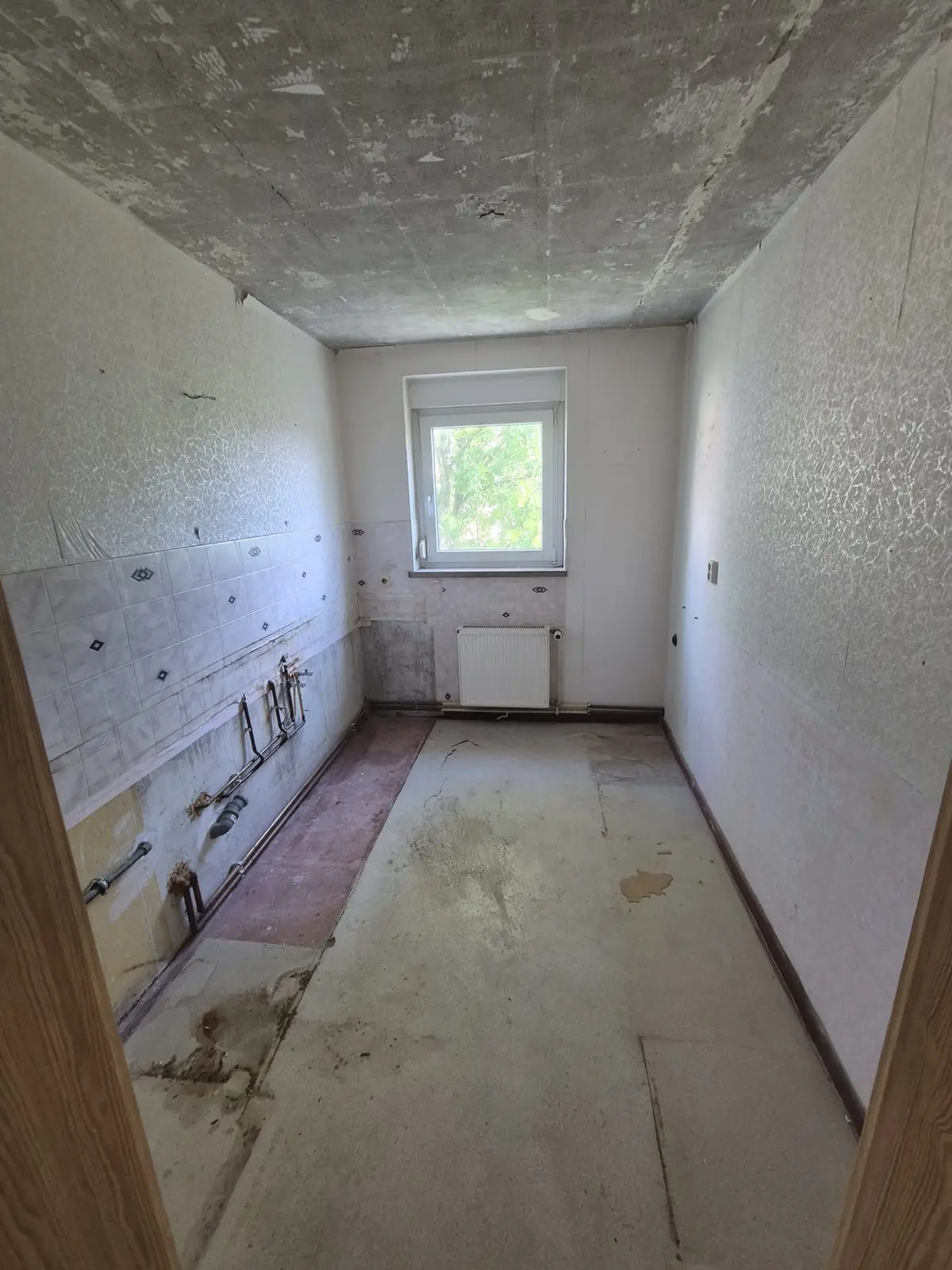 Küche nach der Räumung: Einbauküche ausgebaut, Fliesenspiegel und Anschlüsse offen, Boden frei