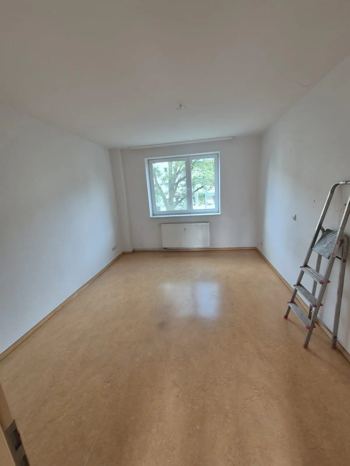 Leergeräumtes Zimmer mit gewischtem Boden, an der Wand steht noch die Trittleiter vom Abbau der letzten Halterungen