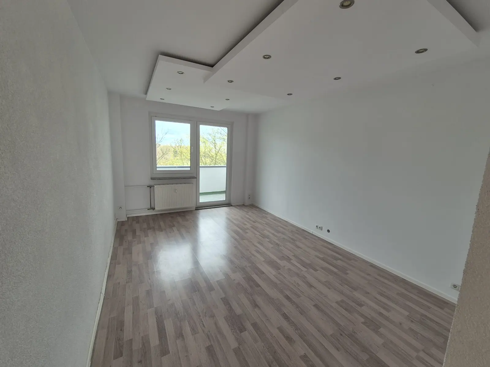 Leerer heller Wohnraum mit Balkontür und Laminatboden nach Abschluss einer Wohnungsauflösung