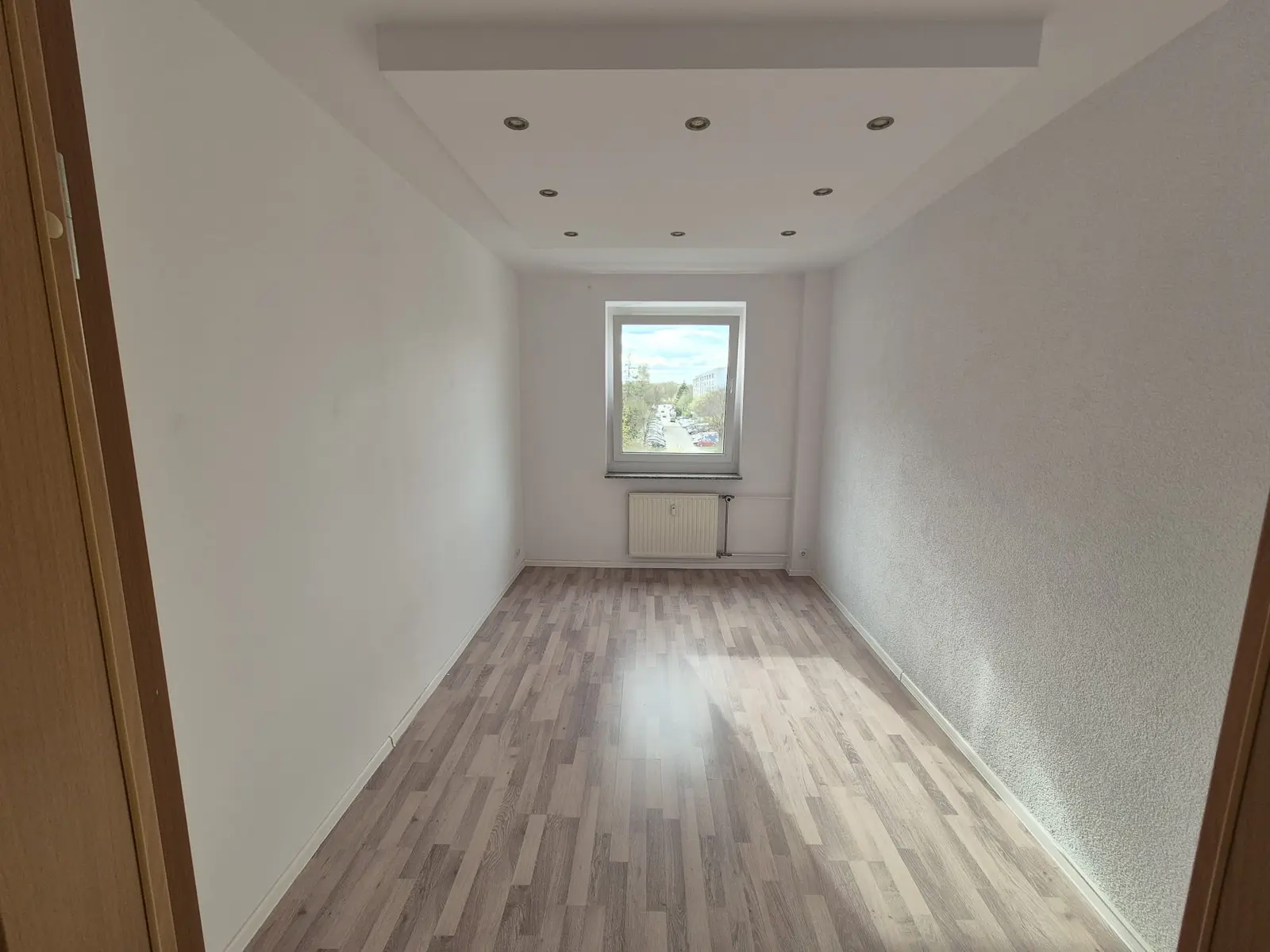 Leergeräumtes Zimmer nach der Räumung: Laminatboden, Fenster und Heizkörper, nichts steht mehr im Raum.