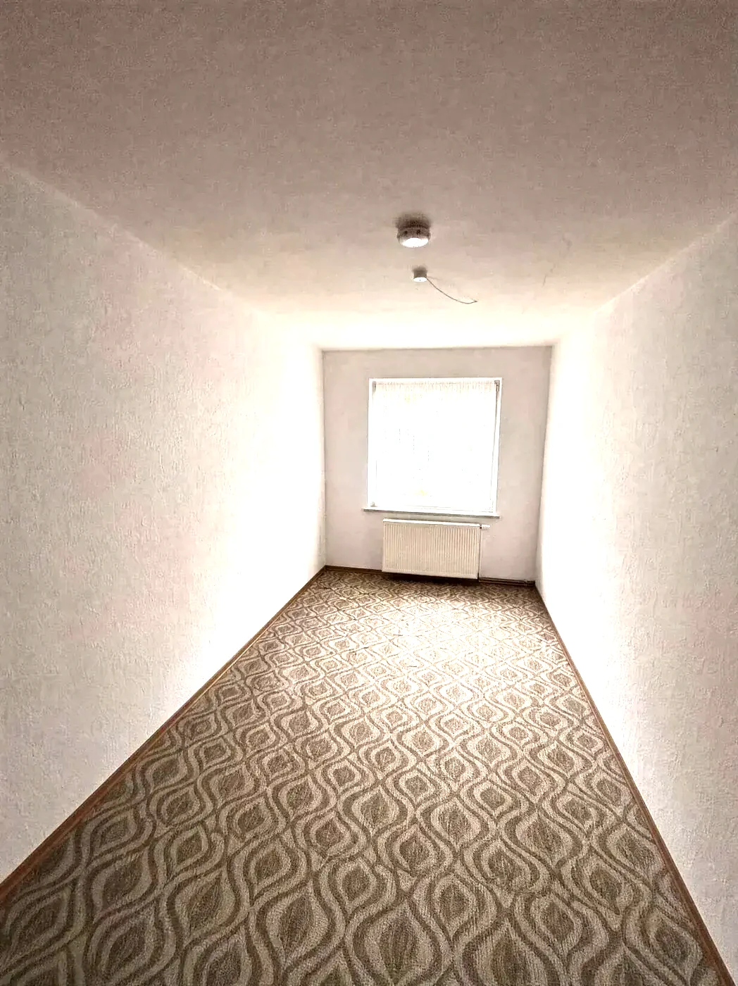 Dasselbe Wohnzimmer leergeräumt, nur Teppichboden und Fenster sind noch zu sehen.